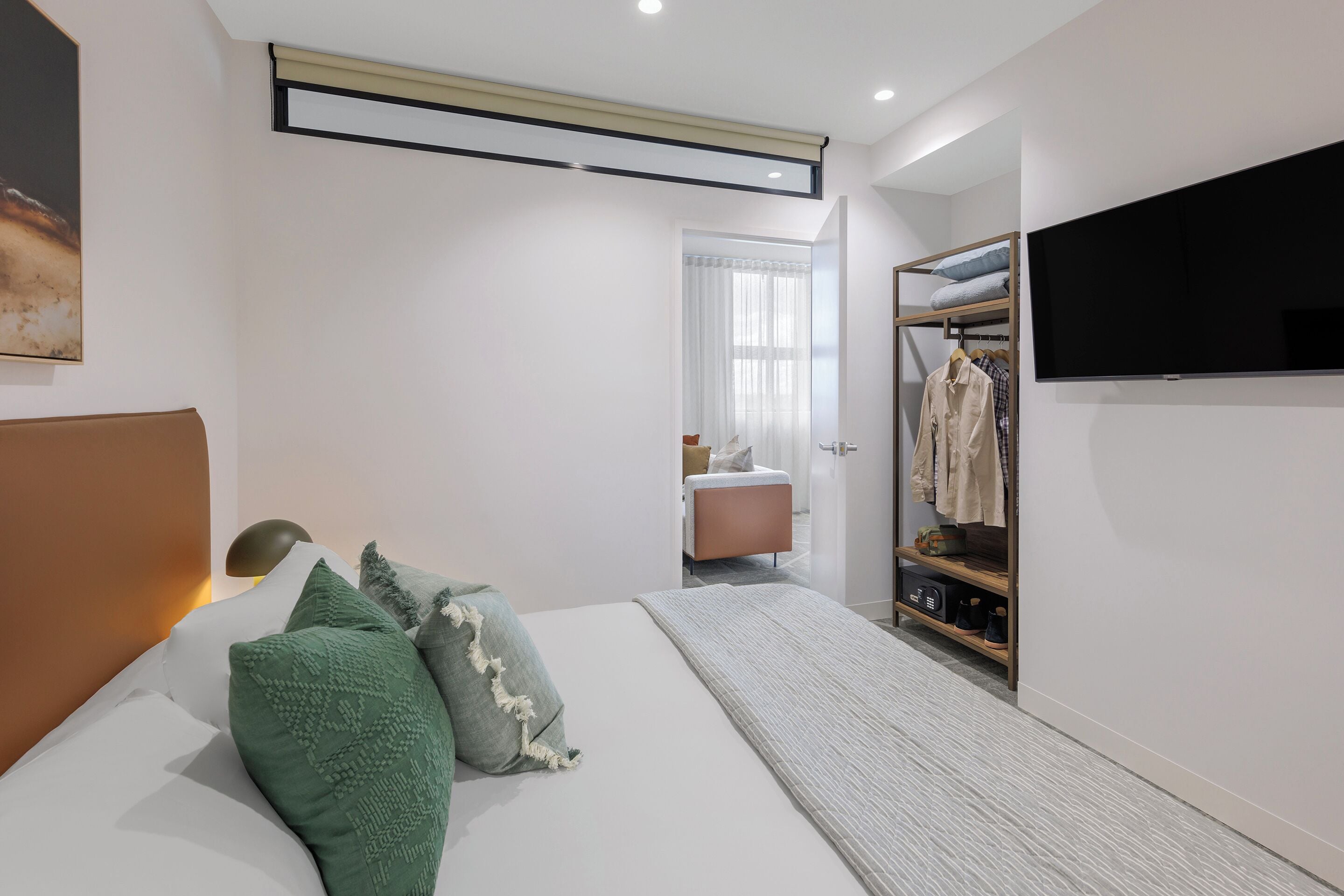 A modern bedroom with a bed, bedside table, and a walk-in closet with a TV.