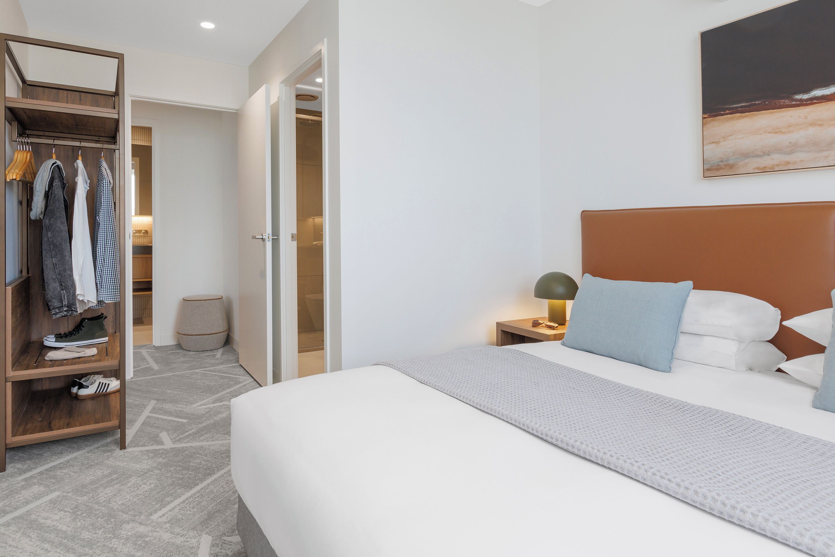 A hotel room with a bed, a nightstand with a lamp, a wardrobe, and a painting on the wall.