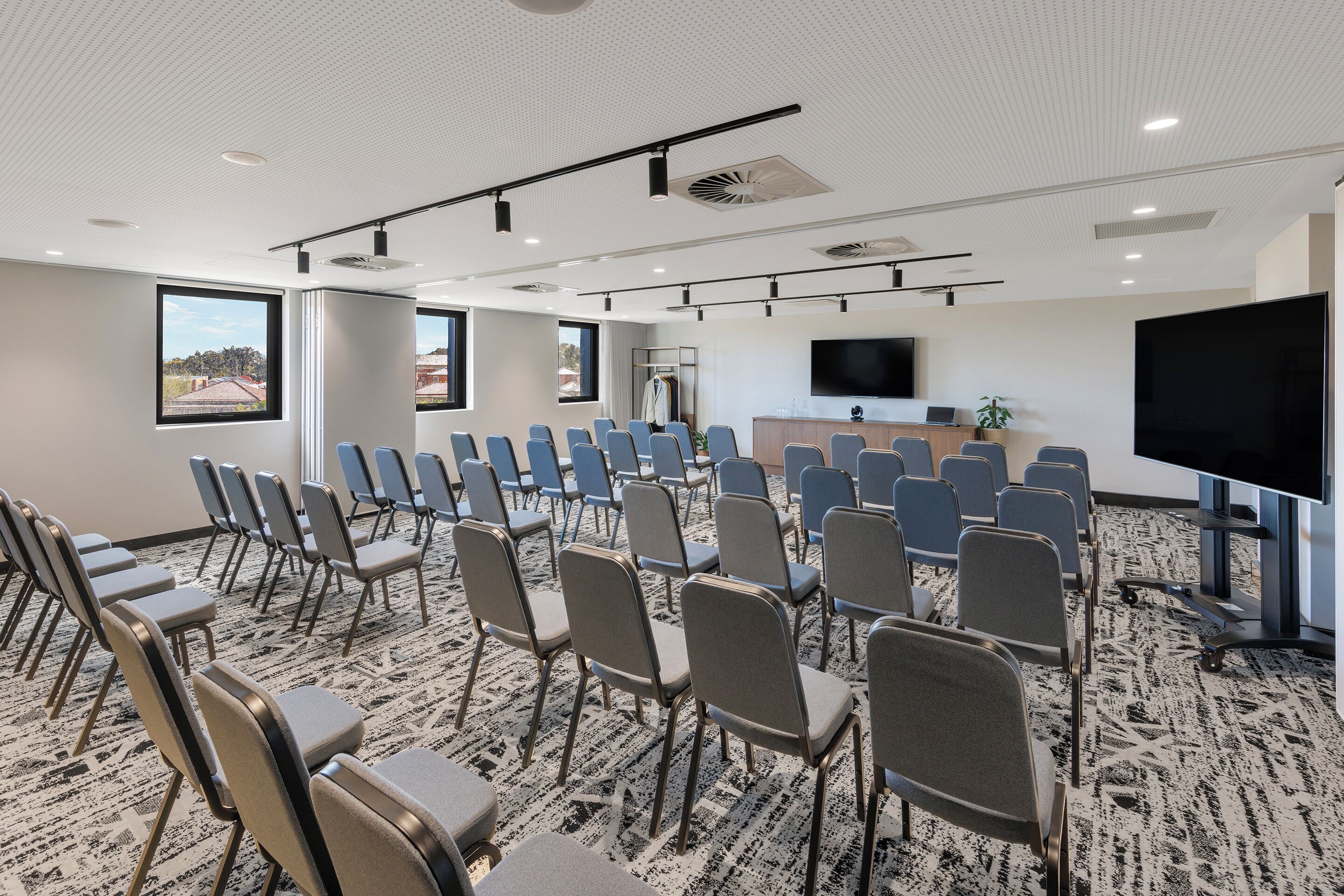 Un salón de conferencias con filas de sillas, una pantalla grande y un mostrador de recepción.