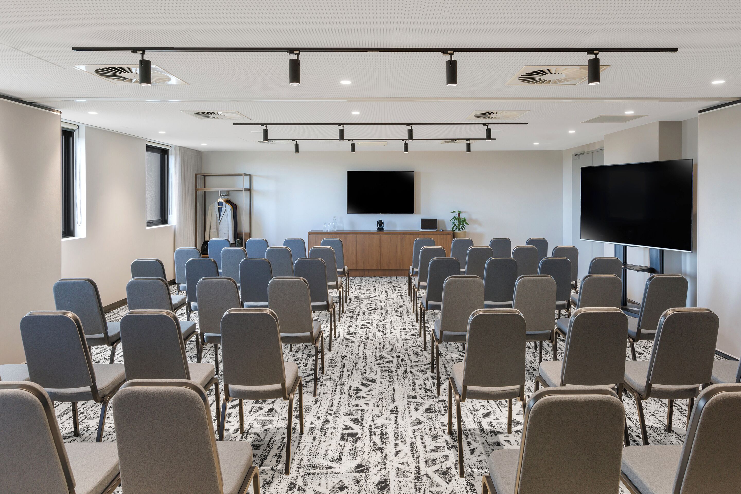Un salón de conferencias con filas de sillas, un televisor de pantalla plana grande, un atril de madera y una planta.