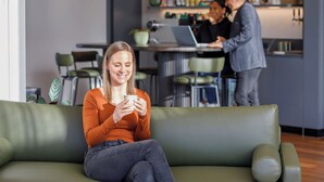 A woman sitting on a green sofa in a modern living room with a laptop on a table in the background. - Punthill Sunshine (Sunshine)