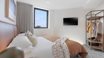 Ein modernes Hotelzimmer mit einem großen Bett, einem an der Wand montierten Fernseher und einem Kleiderständer mit Kleidungsstücken.