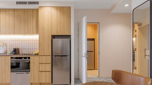A modern kitchen with wooden cabinets, stainless steel appliances, and a dining area with a wooden table and chair. - Punthill Sunshine (Sunshine)