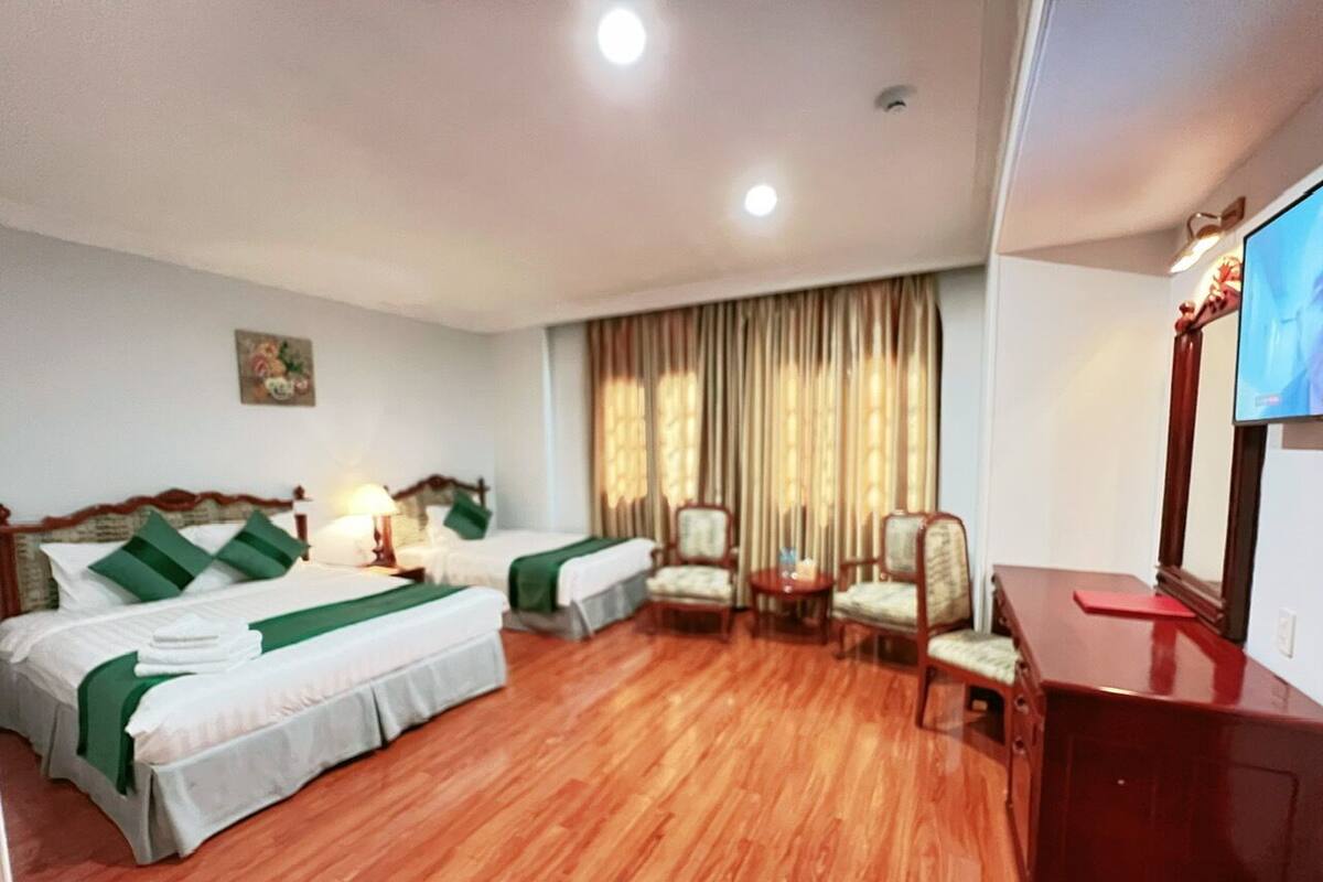 A hotel room with two beds, a desk, a chair, a TV, and a window with curtains.