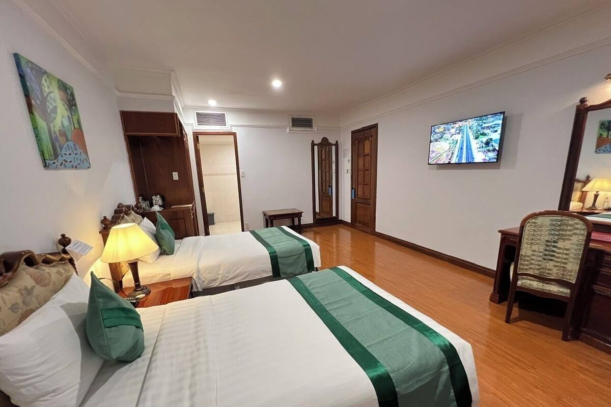 A hotel room with two beds, a desk, a chair, and a television.
