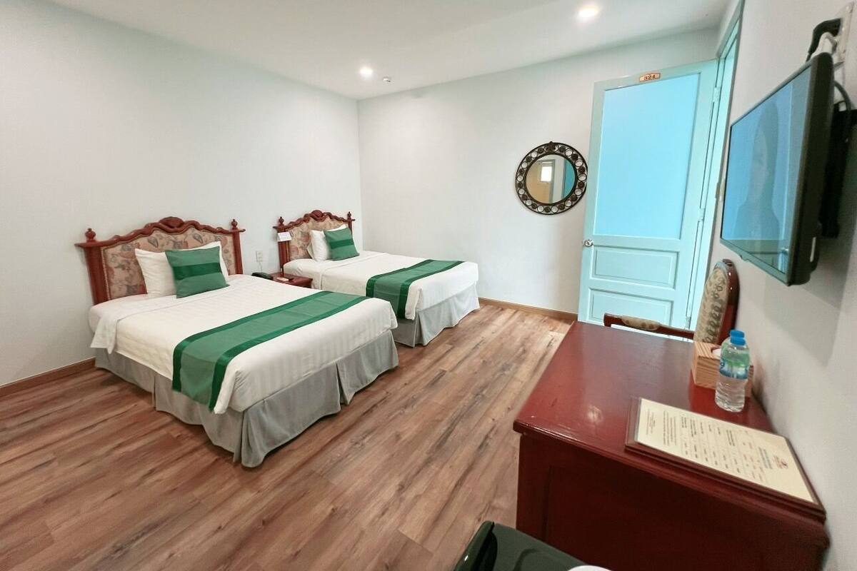 A hotel room with two beds, a desk, a chair, a mirror, and a television.