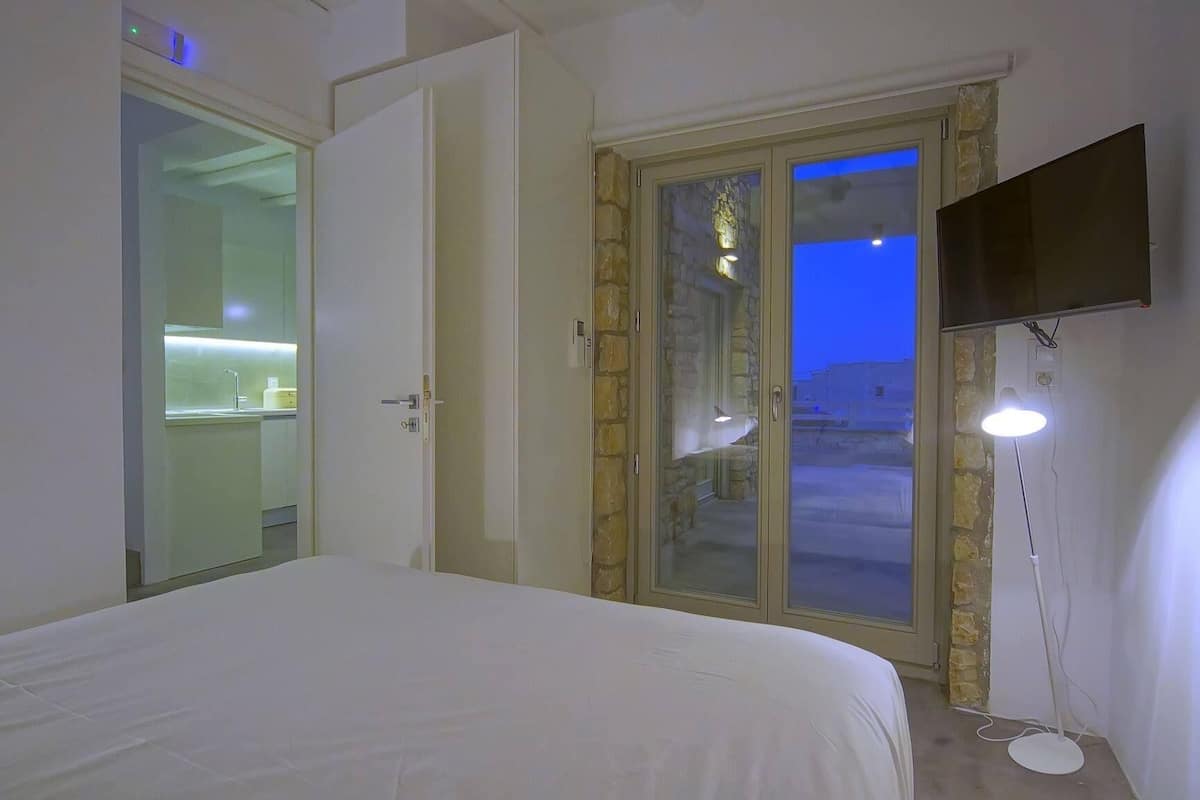 A bedroom with a bed, a TV mounted on the wall, and a door leading to a balcony.