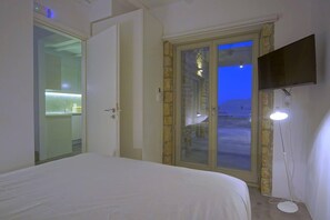 A bedroom with a bed, a TV mounted on the wall, and a door leading to a balcony. - Vista mare villas  (Sitia)