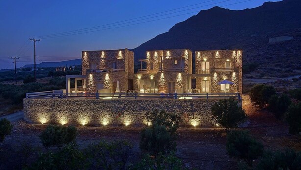 A modern stone building with multiple levels, outdoor seating, and a view of a mountainous landscape. - Vista mare villas (Sitia)