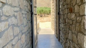 A stone-walled corridor leading to an outdoor area with a view of a hill and sparse vegetation. - Vista mare villas (Sitia)