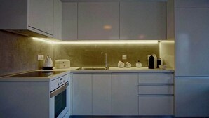 A modern kitchen with white cabinetry, a built-in oven, and a countertop with a kettle and other items. - Vista mare villas (Sitia)