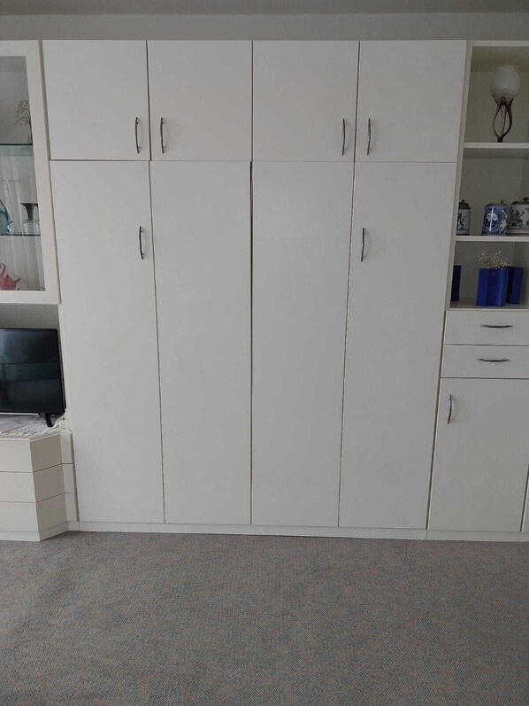Een kamer met een grote witte garderobe, een klein plankje met decoratieve spullen, en een betegelde vloer.