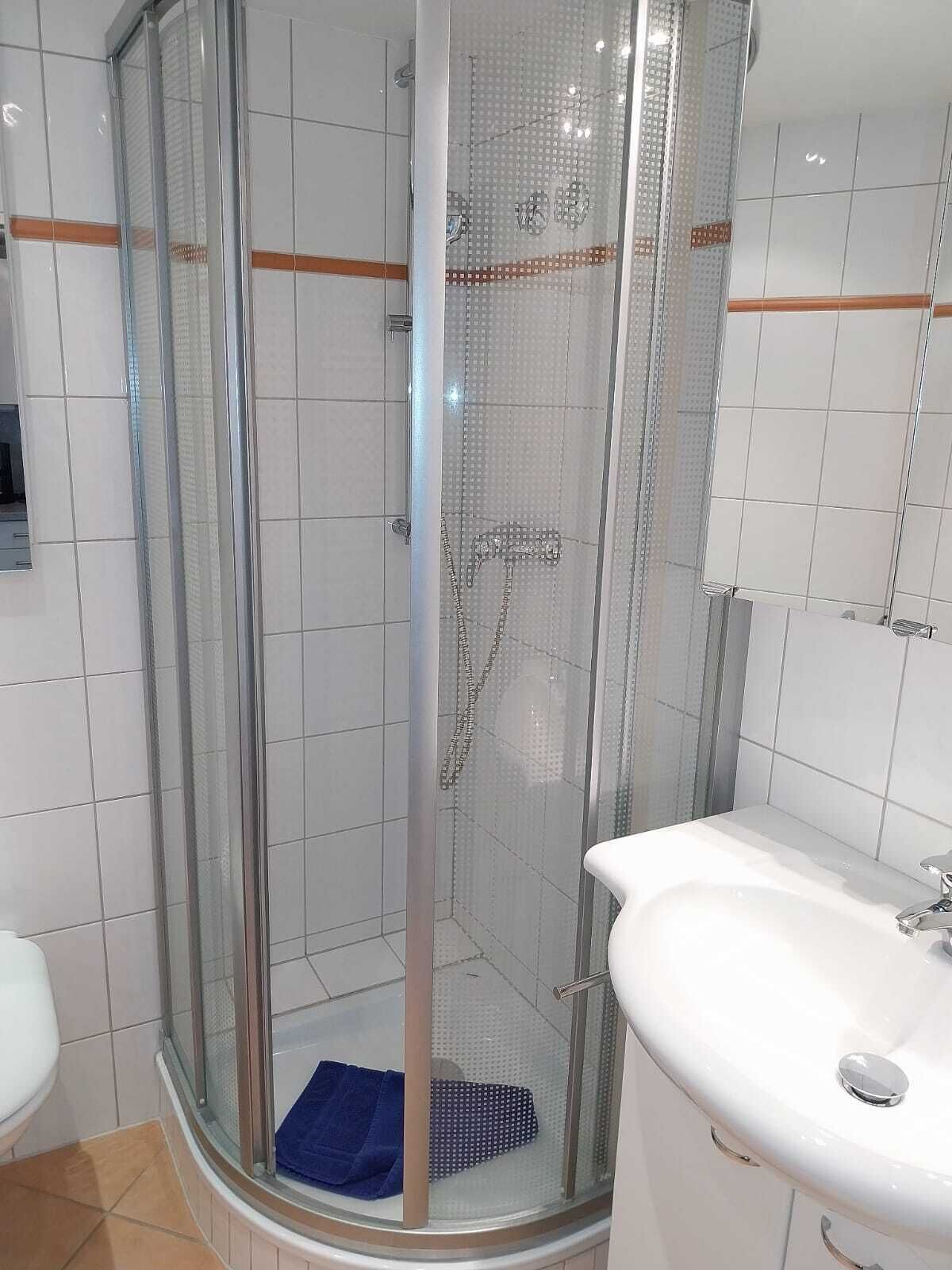 Ein modernes Badezimmer mit einer Duschkabine aus Glas, einem weißen Waschbecken und gefliesten Wänden.