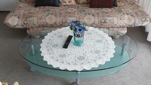 Un saló amb un sofà estampat, una taula de cafè de vidre amb una nostra de punt i un ram de flors.