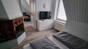 Ett sovrum med en säng, en tv placerad på ett vitt skåp, en byrå i trä och ett fönster med persienner.