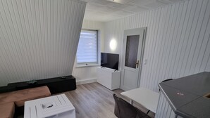 Ett kompakt vardagsrum med en soffa, ett litet vitt bord, en tv och en liten köksdel.