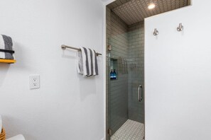 Un baño moderno con cabina de ducha de vidrio, un perchero con toallas a rayas y una pared blanca con un enchufe.