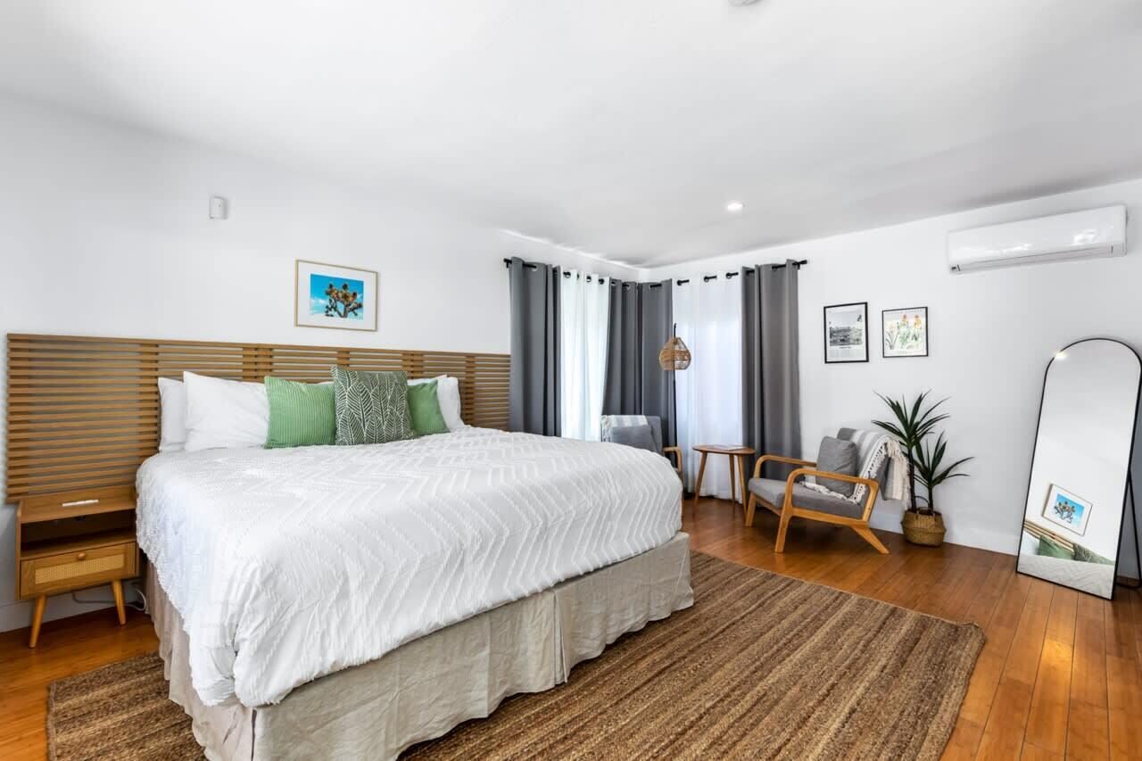 Une chambre moderne avec un grand lit, une tête de lit en bois, une table de chevet, une chaise, une petite table, un miroir et une plante en pot.