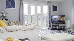 A modern living room with a large TV, comfortable seating, and a view through the glass doors. - Modern Home, 9 beds for Extended Stays, Free Parking (Reading)