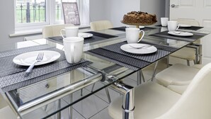 A modern dining area with a glass table, white plates, and a cake on a stand. - Modern Home, 9 beds for Extended Stays, Free Parking (Reading)