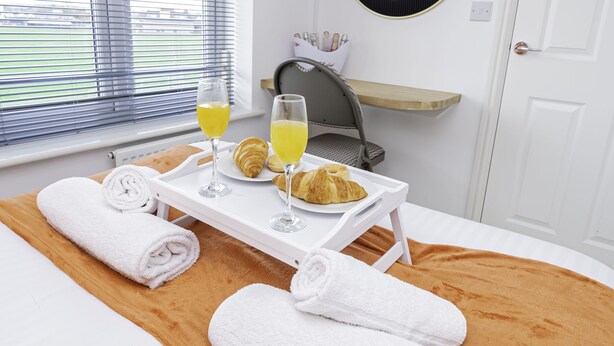 A hotel room with a bed, a tray with croissants and orange juice, a towel, and a window with blinds. - Modern Home, 9 beds for Extended Stays, Free Parking (Reading)