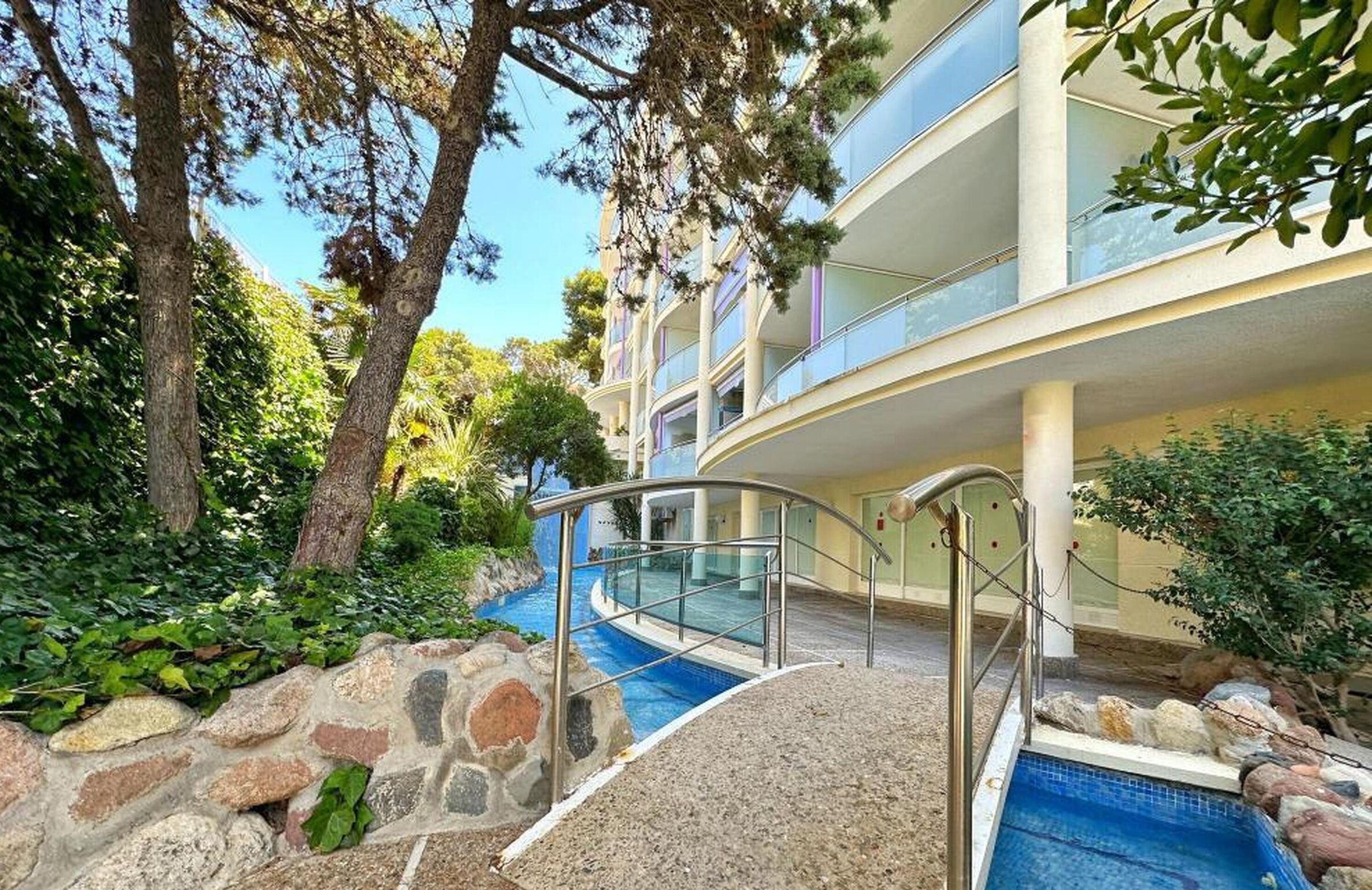 A modern building with a pool, stone pathway, and lush greenery.