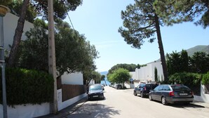 Eine Straße gesäumt von parkenden Autos und Bäumen, mit blauem Himmel und fernen Bergen.