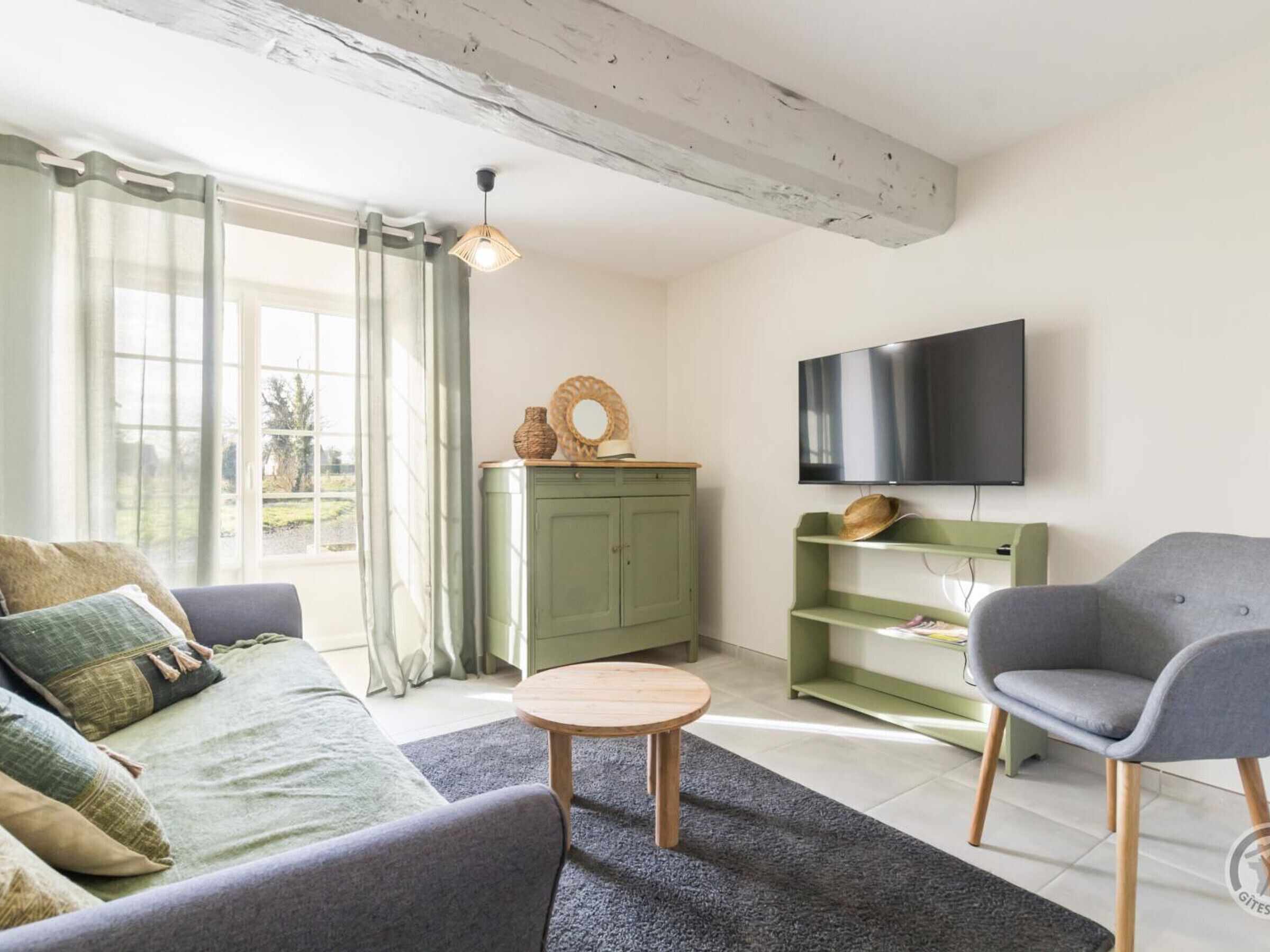 A living room with a sofa, a coffee table, a TV mounted on the wall, and a green cabinet.
