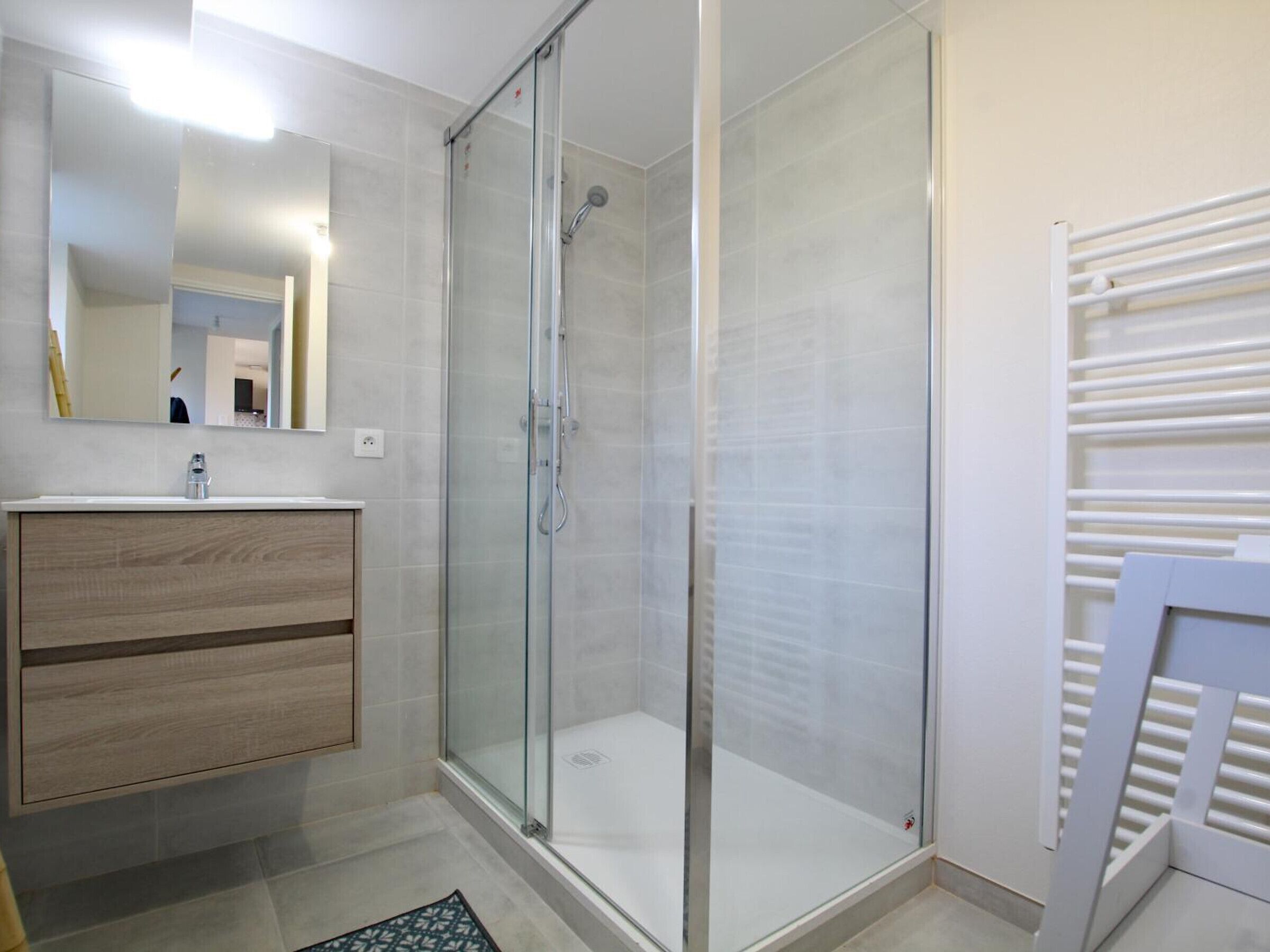 A modern bathroom with a glass-enclosed shower, a wooden vanity, and a white towel rack.