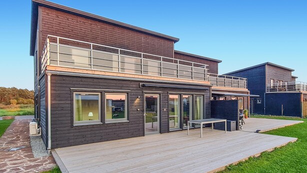 A modern two-story house with a balcony, large windows, and a wooden deck.