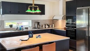 A modern kitchen with dark cabinetry, a central island with two chairs, a stainless steel refrigerator, and a coffee maker.