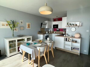 A modern kitchen with white cabinetry, a dining table with chairs, and a hanging light fixture. - 3-star apartment in Saint Jean de Monts, 5 people, parking, sea view (Saint-Jean-de-Monts)