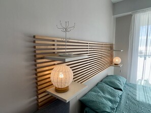 A modern bedroom with a slatted headboard, a bedside table with a lamp, and a bed with a patterned blanket. - 3-star apartment in Saint Jean de Monts, 5 people, parking, sea view (Saint-Jean-de-Monts)