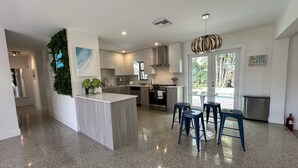 A modern kitchen with a central island, bar stools, and a view to the outdoors.
