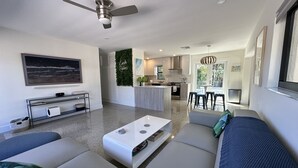 A modern living room with a sofa, coffee table, and a TV. There is a kitchen area with a dining table and chairs.