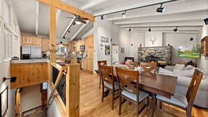 Een ruime keuken met houten kasten, een eethoek met een houten tafel en stoelen, en een woonkamer met een stenen open haard en een bank.