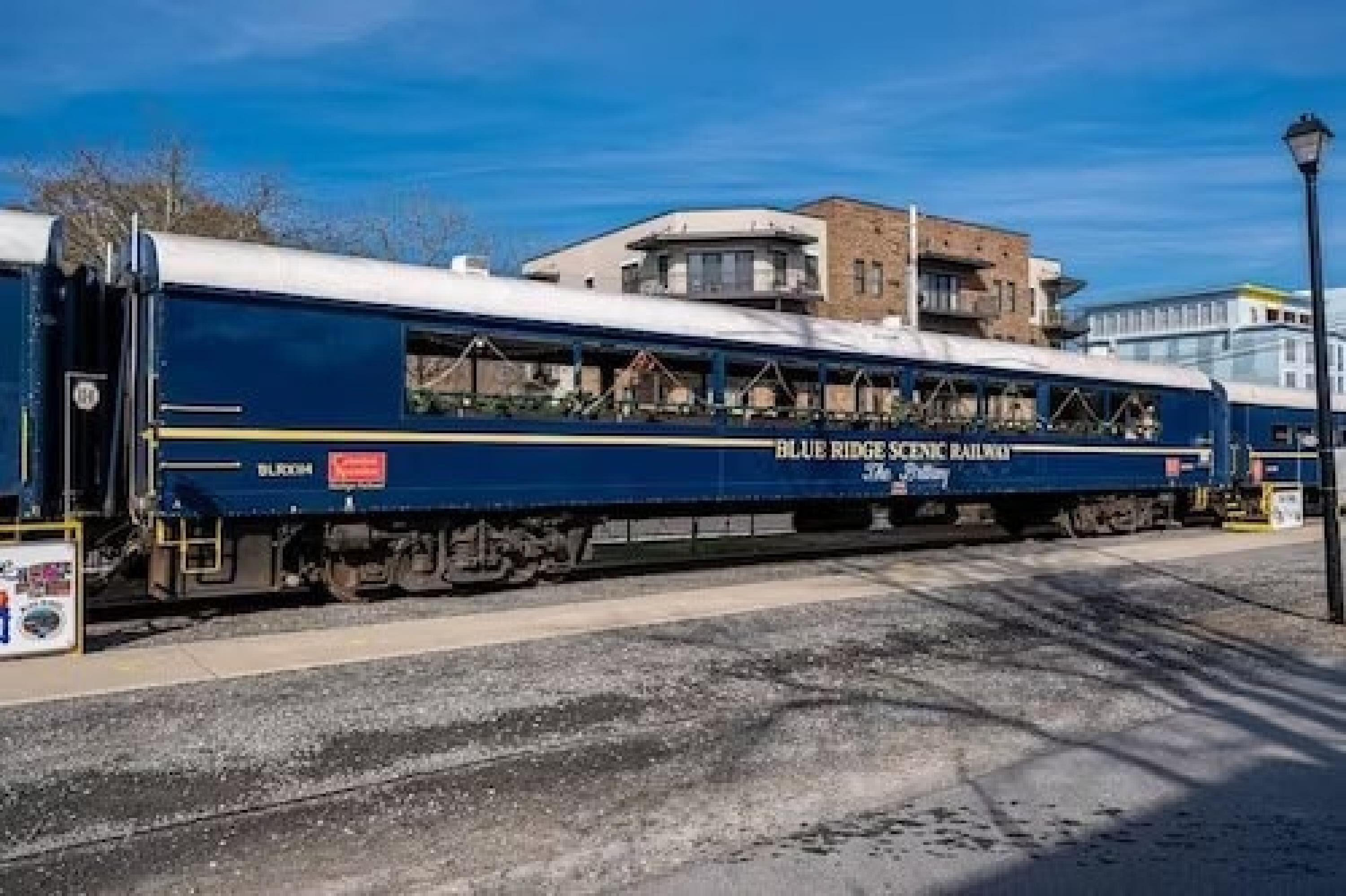 Ein Zug mit der Aufschrift "BLUE RIDGE RAILROAD" am Wagen, geparkt auf Gleisen, mit Gebäuden im Hintergrund.