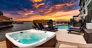 A pool area with lounge chairs and hot tubs, overlooking a body of water with a sunset sky.