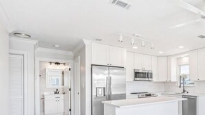 A modern kitchen with white cabinetry, stainless steel appliances, and a central island. - Modern Poolside Villa-steps to Beach (Panama City Beach)