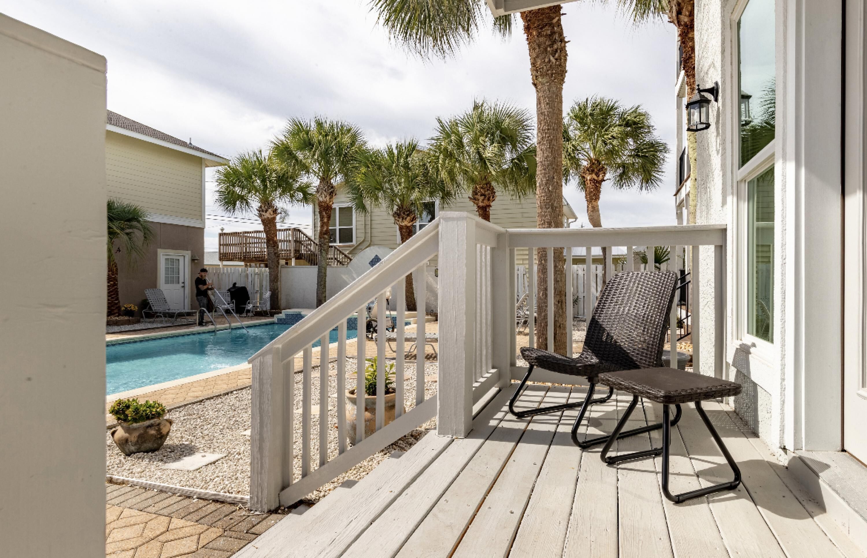 A wooden deck with a pool, palm trees, and a white railing.