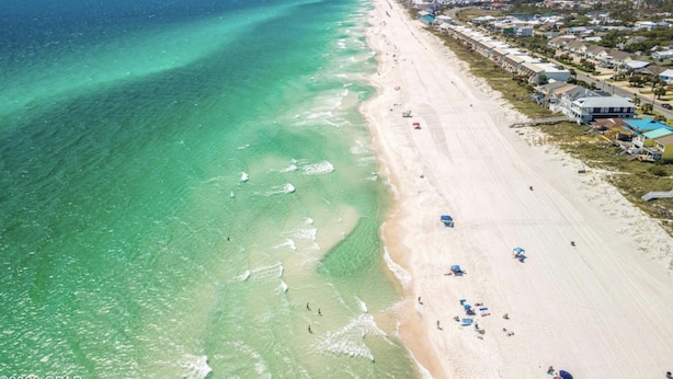 An aerial view of a beach with clear turquoise waters, a sandy shore, and buildings along the coastline. - Modern Poolside Villa-steps to Beach (Panama City Beach)