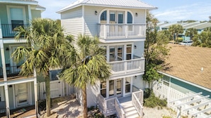 A two-story beachfront house with a balcony, palm trees, and a sandy beach in the background. - Modern Poolside Villa-steps to Beach (Panama City Beach)