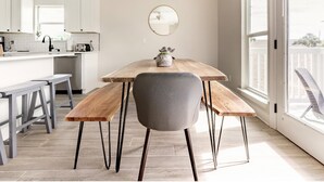 A modern kitchen with white cabinets, a wooden dining table, and a gray chair. - Modern Poolside Villa-steps to Beach (Panama City Beach)