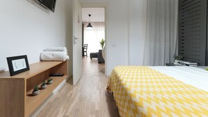 Camera da letto moderna con pavimento in legno, un letto con copriletto giallo a motivi decorativi, un comodino con una cornice e una piccola pianta.