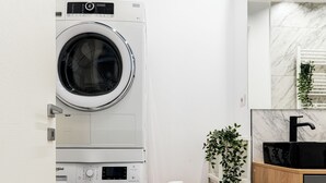 Una lavanderia piccola e funzionale con due lavatrici affiancate, un ripiano con una pianta e un lavandino nero in una cucina moderna.