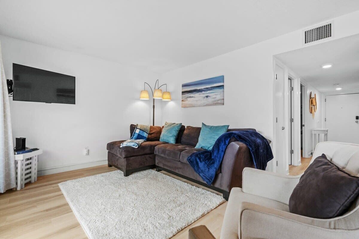 A living room with a sectional sofa, a white rug, a flat-screen TV, and a floor lamp.