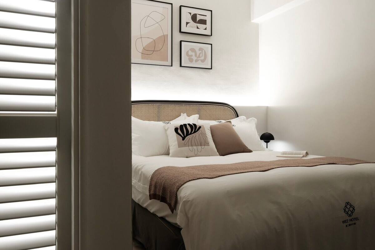 A neatly arranged bedroom with a bed, pillows, a bedside lamp, and wall art.