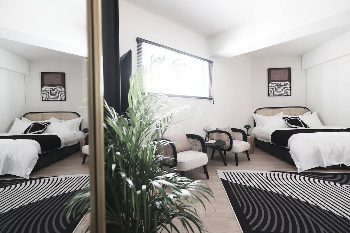 A modern bedroom with two beds, a seating area, and a large window.