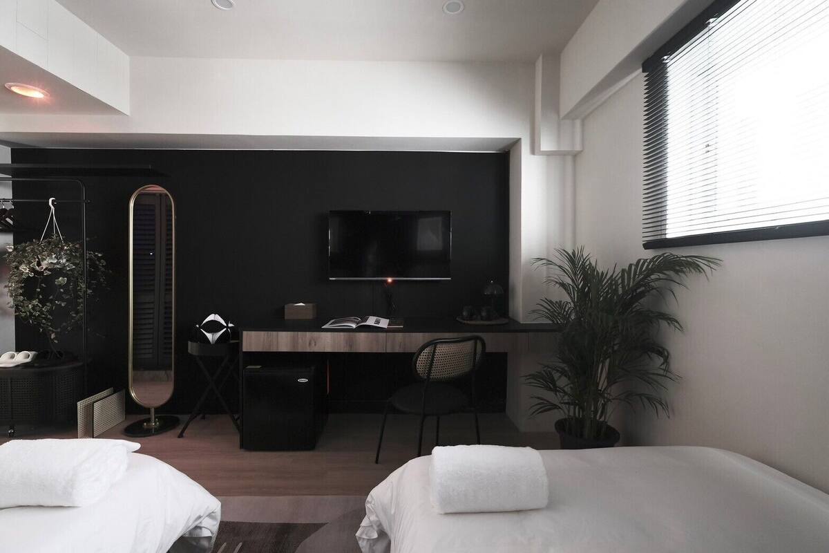 A modern hotel room with a bed, a desk with a chair, a TV, and a large mirror.