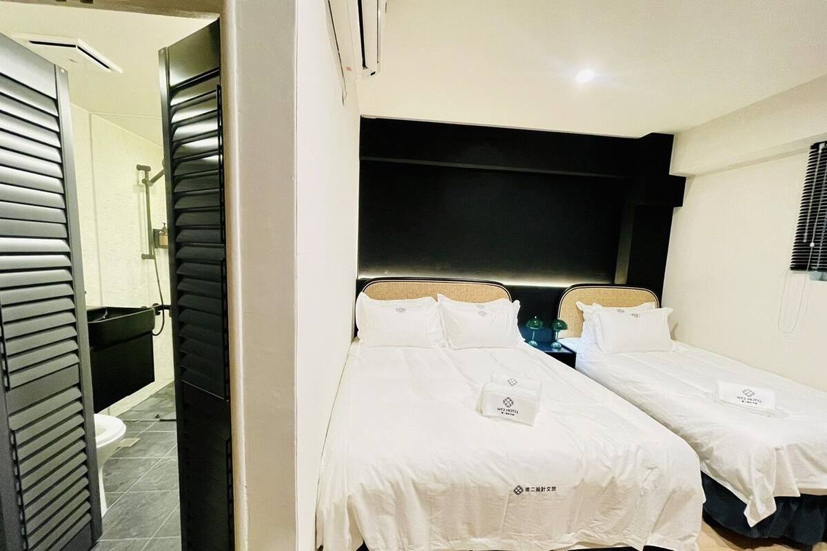 A hotel room with two single beds, a large mirror, and a view of the bathroom.